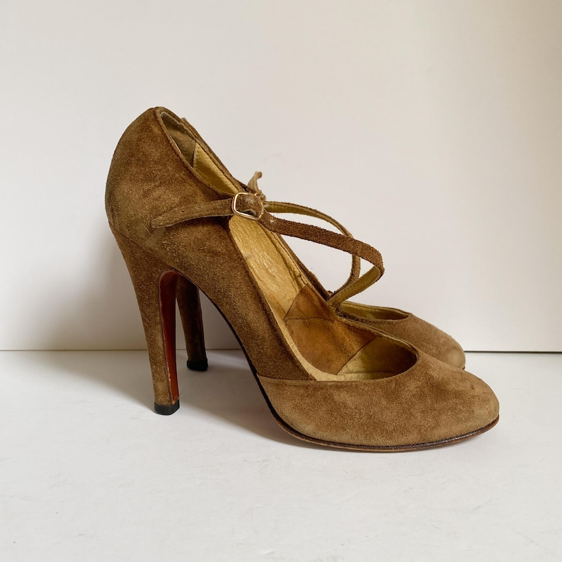 May include: A pair of brown suede heeled shoes with a strap across the ankle and a buckle closure.