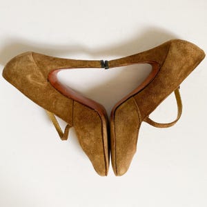 May include: A pair of brown suede heeled shoes with ankle straps. The shoes have a pointed toe and a high heel.