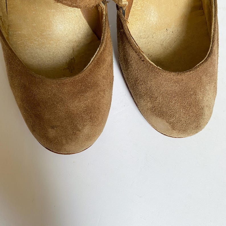 May include: A pair of brown suede heeled shoes with a strap across the top.