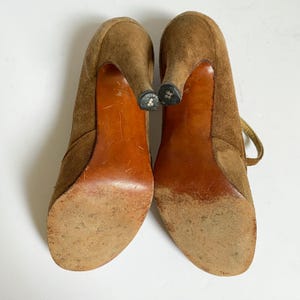 May include: A pair of brown suede high-heeled shoes with a lace-up detail. The shoes have a pointed toe and a high stiletto heel.