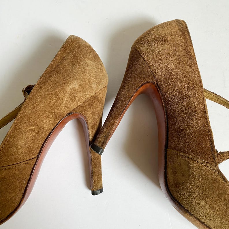 May include: A pair of brown suede high-heeled shoes with ankle straps. The shoes have a pointed toe and a stiletto heel.
