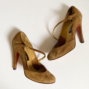 May include: A pair of brown suede heeled shoes with ankle straps. The shoes have a pointed toe and a high heel.