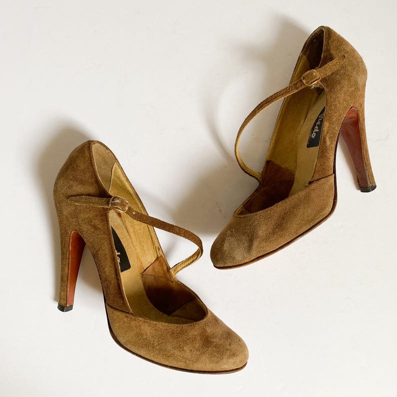 May include: A pair of brown suede heeled shoes with ankle straps. The shoes have a pointed toe and a high heel.
