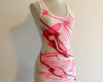 May include: White tank top with a pink and red abstract design. The design features a large, abstract shape in the center of the tank top. The text "Black" is visible on the right side of the tank top.