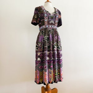 Könnte beinhalten: Ein lila, schwarzes und grünes Paillettenkleid mit Blumenmuster und einem Perlenbesatz am Ausschnitt. Das Kleid hat kurze Ärmel und eine Midi-Länge.