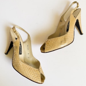 May include: A pair of beige snakeskin peep-toe heeled sandals with slingback straps. The sandals are labelled "SW2380 8 7" and "Stuart Weitzman".