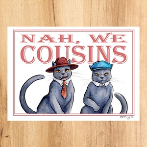 Puede incluir: Impresión rectangular con dos gatos grises con sombreros y corbatas. El texto rojo dice "NAH, WE COUSINS". Un gato lleva sombrero y corbata rojos, el otro un sombrero azul. La impresión tiene un borde blanco sobre un fondo de madera.