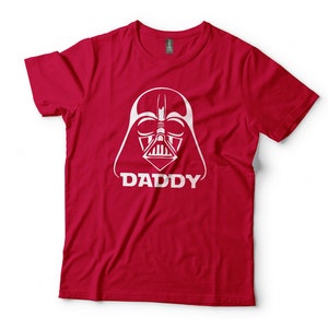 May include: Red t-shirt with a white graphic of Darth Vader's face and the word "DADDY" underneath.