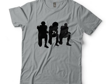 May include: A gray t-shirt with a black silhouette of three football players kneeling.