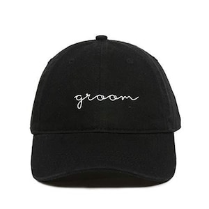 May include: Black baseball cap with a white embroidered cursive word "groom" on the front.