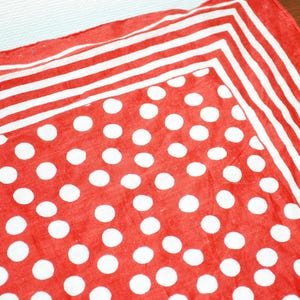 Könnte beinhalten: Rot-weiß gemusterter Stoff. Der Stoff hat ein Tupfenmuster in Rot mit weißen Punkten und einen gestreiften Rand in Rot und Weiß. Der Stoff ist wahrscheinlich ein Schal oder ein Bandana.