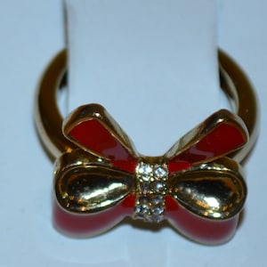 May include: A gold ring with a red enamel bow and clear rhinestones.