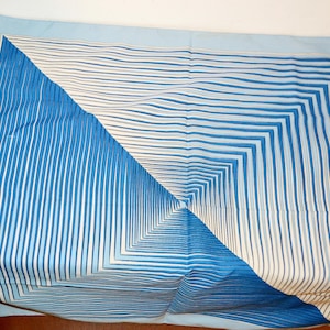 Könnte beinhalten: Ein hellblaues quadratisches Tuch mit geometrischem Design. Das Tuch hat ein zentrales quadratisches Muster aus blauen und weißen Linien mit einem hellblauen Rand. Die Linien erzeugen eine optische Täuschung von Tiefe und Dimension.