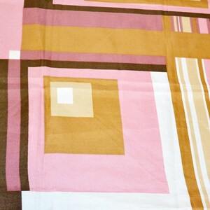 Könnte beinhalten: Nahaufnahme eines Stoffes mit geometrischem Muster in Rosa, Braun und Gold. Das Design zeigt Quadrate, Rechtecke und Streifen, die eine Retro-Ästhetik erzeugen. Der Stoff wirkt weich, möglicherweise für Bettwäsche oder Polsterung.