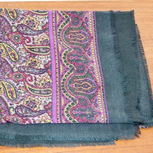Könnte beinhalten: Ein gefalteter Schal mit Paisley-Muster in Lila, Rot und Gelb. Der Schal hat einen dunkelgrünen Rand mit Fransen. Der Schal ist aus einem weichen Material gefertigt.