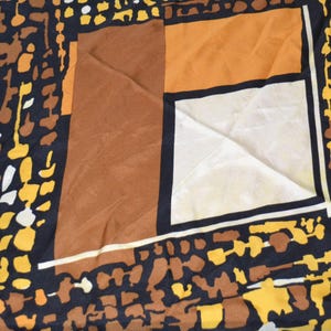 Könnte beinhalten: Ein gemusterter Schal mit geometrischem Design. Der Schal weist eine Kombination aus Farben auf, darunter Schwarz, Braun, Gelb und Weiß. Das Design umfasst ein Quadrat mit braunen, orangefarbenen und weißen Abschnitten.