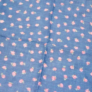 Könnte beinhalten: Ein blauer Stoff mit einem Muster aus kleinen rosa Rosen. Der Stoff hat einen Fransenrand und ist wahrscheinlich ein Schal oder ein ähnliches Textil. Die Rosen sind gleichmäßig verteilt.