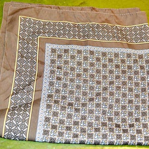 Könnte beinhalten: Ein braunes Einstecktuch mit einem geometrischen Muster in Braun-, Gelb- und Weißtönen. Das Einstecktuch hat einen gemusterten Rand und ein sich wiederholendes Blumendesign in der Mitte. Der Stoff ist gefaltet.