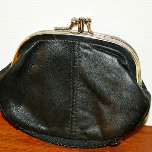 May include: A black leather coin purse with a metal clasp and frame. The purse has a rounded shape and a zipper closure at the bottom. The leather appears to be slightly textured.
