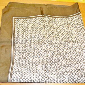 May include: A brown silk scarf with a white geometric pattern. The scarf has a brown border.