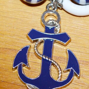 Op de afbeelding: Een blauwe en zilveren ankerbedel met een touwontwerp. Het anker is een populair nautisch symbool.