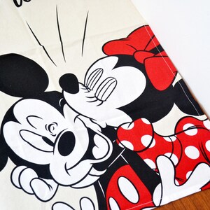 May include: A cream-colored fabric runner featuring a black and white graphic of Mickey Mouse and Minnie Mouse kissing. Minnie wears a red dress with white polka dots and a matching red bow. The text "the" is partially visible at the top edge.