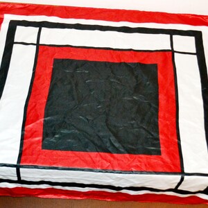 Könnte beinhalten: Ein quadratischer Schal in Rot, Schwarz und Weiß mit einem geometrischen Design. Er hat einen roten Rand, ein weißes und schwarzes rechteckiges Muster und ein schwarzes Quadrat in der Mitte. Der Schal ist aus glänzendem Material.