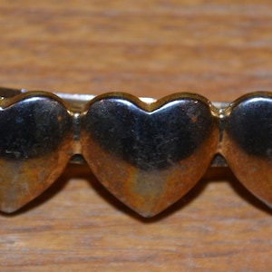 Op de afbeelding: Een gouden haarspeld met vijf hartvormige bedels. De speld is ontworpen om haar op zijn plaats te houden.