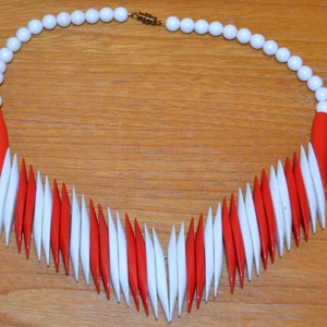 Könnte beinhalten: Eine rot-weiße Perlenkette mit einem goldenen Verschluss. Die Perlen sind in einem Chevron-Muster angeordnet.