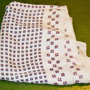 Könnte beinhalten: Weißer Stoff mit einem sich wiederholenden Muster aus kleinen roten und blauen Blumenmustern. Der Stoff ist gefaltet und zeigt das Muster über die gesamte Oberfläche. Der Hintergrund ist einfarbig grün.