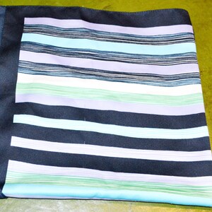 May include: A folded navy blue silk scarf with a striped pattern in shades of blue, green, white, and lavender. The scarf has a solid navy blue border and a smooth, shiny texture.