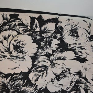 May include: A rectangular scarf featuring a high-contrast black and white floral pattern. The design consists of large, detailed blossoms and leaves printed in black ink against a solid white background, finished with a solid black border.