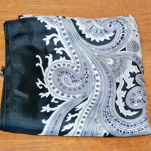 Könnte beinhalten: Gefalteter schwarz-weißer Schal mit Paisley-Muster. Der Schal hat ein detailliertes Design mit wirbelnden Mustern in Grau- und Weißtönen auf schwarzem Hintergrund. Der Schal ist aus seidigem Material gefertigt.