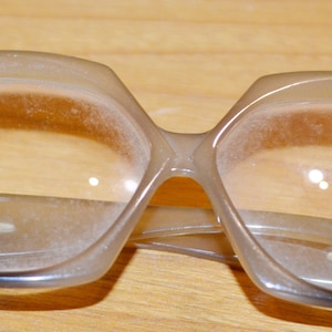 May include: A pair of dusty, clear, plastic framed glasses with a black bridge and arms.