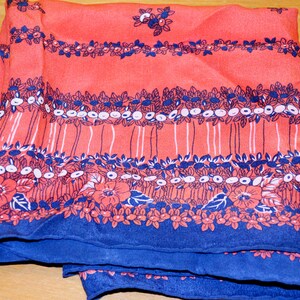 May include: A red silk scarf with a blue floral pattern. The pattern features small white flowers and leaves.