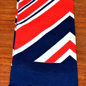 May include: A blue, red and white striped scarf with a fringed edge. The scarf is folded in half and has a diagonal pattern.