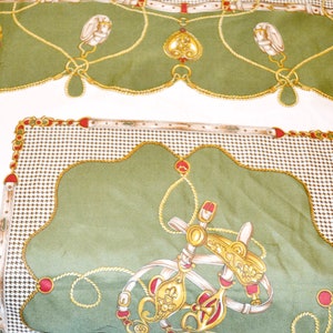 May include: Green and white fabric with a repeating pattern of gold chains, red jewels, and horse-related imagery. The fabric has a satin-like sheen.