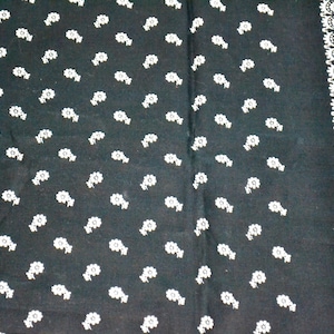 May include: A black fabric bandana featuring a repeating pattern of small white flower motifs across the main surface and a distinct vertical border design composed of intricate white circular and geometric shapes along the right edge.