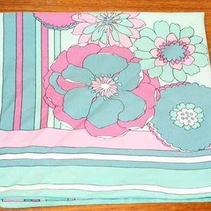 Könnte beinhalten: Ein gefaltetes Textil mit einem floralen Muster in Rosa, Türkis und Weiß. Das Design umfasst große stilisierte Blumen und vertikale Streifen, die eine Retro-Ästhetik erzeugen. Der Stoff ist wahrscheinlich Baumwolle oder ein ähnliches Material.