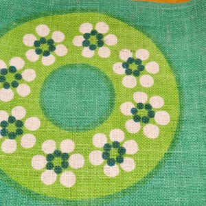 May include: Green fabric with a white and green floral pattern. The pattern features a ring of white flowers with green centres, surrounding a larger green circle.
