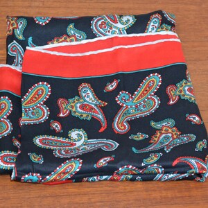 May include: A black silk scarf with a paisley pattern in red, blue and yellow. The scarf has a red border with a white trim.