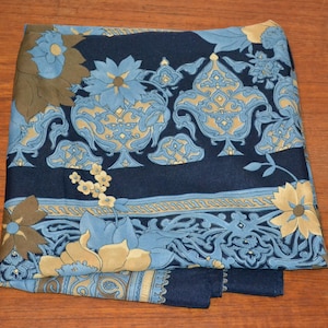 Könnte beinhalten: Gefalteter marineblauer Schal mit einem Blumenmuster in Hellblau-, Beige- und Brauntönen. Der Schal weist ein sich wiederholendes Design aus stilisierten Blumen und ornamentalen Formen auf, wodurch eine Vintage-Ästhetik entsteht. Der Schal liegt auf einer Holzoberfläche.
