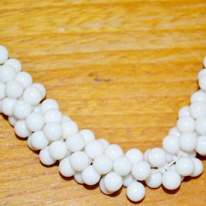 Könnte beinhalten: Eine weiße Perlenkette aus kleinen, runden Perlen. Die Kette ist in einem geschichteten, kaskadierenden Muster angeordnet.