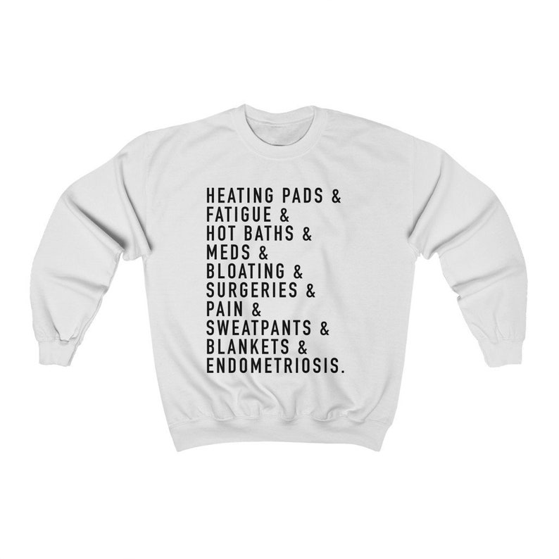 May include: White sweatshirt with black text that reads "HEATING PADS & FATIGUE & HOT BATHS & MEDS & BLOATING & SURGERIES & PAIN & SWEATPANTS & BLANKETS & ENDOMETRIOSIS."