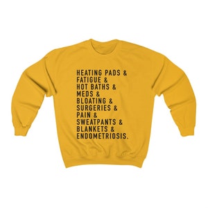 May include: Yellow sweatshirt with black text that reads "HEATING PADS & FATIGUE & HOT BATHS & MEDS & BLOATING & SURGERIES & PAIN & SWEATPANTS & BLANKETS & ENDOMETRIOSIS."