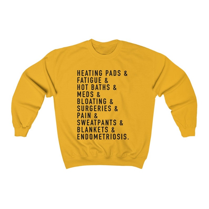 May include: Yellow sweatshirt with black text that reads "HEATING PADS & FATIGUE & HOT BATHS & MEDS & BLOATING & SURGERIES & PAIN & SWEATPANTS & BLANKETS & ENDOMETRIOSIS."