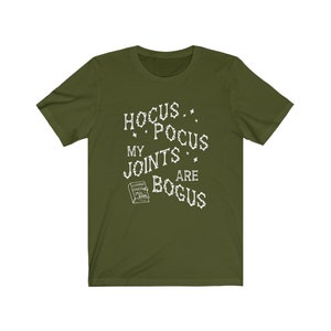May include: A green t-shirt with a white graphic that says "Hocus Pocus My Joints Are Bogus" with a small book image that says "Chronic Haxing Spell Book".