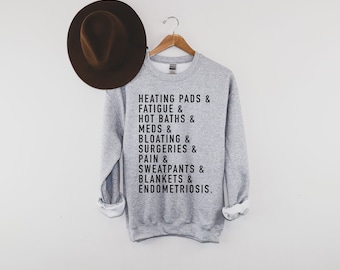 Puede incluir: Sudadera gris con texto negro que dice "HEATING PADS & FATIGUE & HOT BATHS & MEDS & BLOATING & SURGERIES & PAIN & SWEATPANTS & BLANKETS & ENDOMETRIOSIS."