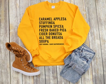 May include: A yellow sweatshirt with the text "CARAMEL APPLES & STUFFING & PUMPKIN SPICE & FRESH BAKED PIE & CIDER DONUTS & ALL THE BREAD & SOUP & JUST KIDDING, I HAVE GASTROPARESIS." printed on the front.