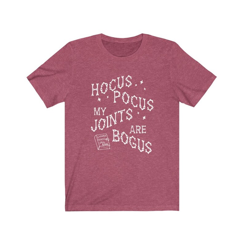 May include: A heather red t-shirt with a white graphic that says "Hocus Pocus My Joints Are Bogus" with a small book graphic that says "Chronic Pain Spell Book".